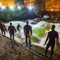 Los surfistas se paran con sus tablas a orillas de la ola artificial del Eisbach en el Jardín Inglés. | Foto:Peter Kneffel / DPA