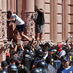 Fans climb up the facade of the Casa Rosada government house as they wait to enter to pay tribute to late football legend Diego Armando Maradona, in Buenos Aires, on November 26, 2020. 