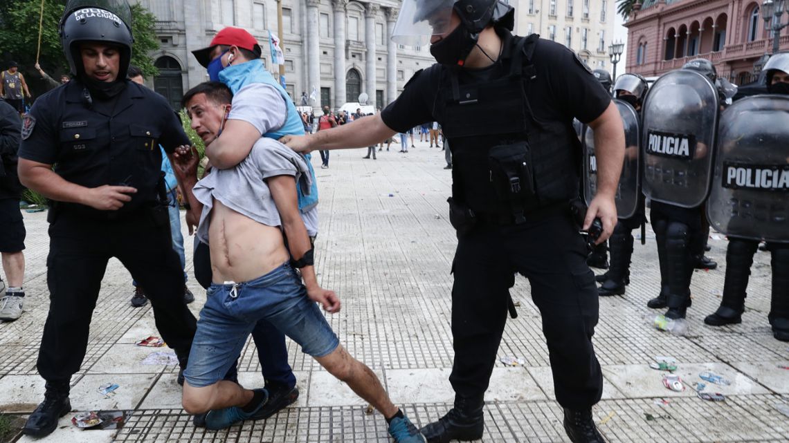 Police detain a man during clashes while fans wait to enter the Government House to pay tribute to late football legend Diego Armando Maradona in Buenos Aires, on November 26, 2020.