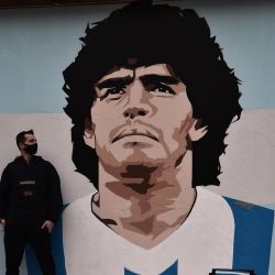 El artista callejero Stilos Ilias posa junto a su graffiti que representa a la leyenda del fútbol argentino Diego Maradona, pintado en una pared de una escuela primaria en el barrio de Kalamaria en Tesalónica. | Foto:Sakis Mitrolidis / AFP