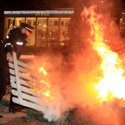 Un hombre sostiene una plataforma de madera en llamas cerca de un árbol de Navidad en llamas mientras los manifestantes se enfrentan con la policía antidisturbios frente al edificio del primer ministro albanés durante los enfrentamientos en Tirana. | Foto:Stringer / AFP