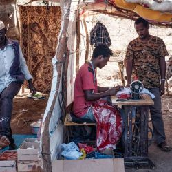 El sastre de refugiados etíope Omar Ibrahim, que huyó del conflicto de Tigray, trabaja con una máquina de coser alquilada en una aldea sudanesa vecina, en su tienda de taior improvisada en el campo de refugiados de Um Raquba en el estado de Gedaref, en el este de Sudán. | Foto:Yasuyoshi Chiba / AFP