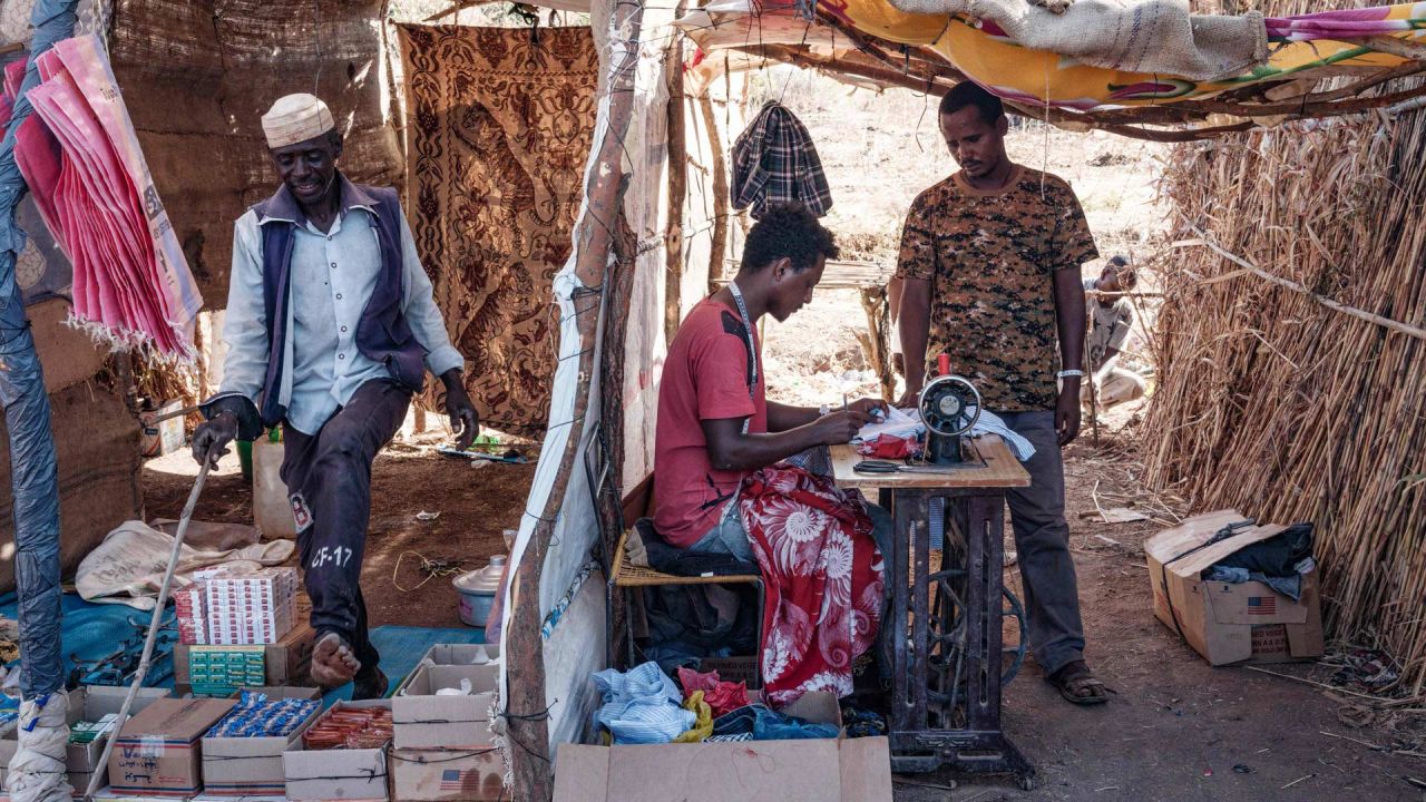 El sastre de refugiados etíope Omar Ibrahim, que huyó del conflicto de Tigray, trabaja con una máquina de coser alquilada en una aldea sudanesa vecina, en su tienda de taior improvisada en el campo de refugiados de Um Raquba en el estado de Gedaref, en el este de Sudán. | Foto:Yasuyoshi Chiba / AFP