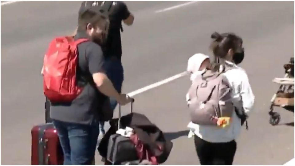 Pasajeros caminan por la autopista con niños en brazos y equipaje para no perder su vuelo.