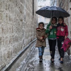 Siria, Ariha: Tres niñas sirias usan un paraguas para protegerse de la lluvia mientras caminan por un callejón cerca de un mercado local en medio de un clima frío. Siria, devastada por la guerra, experimenta veranos muy calurosos e inviernos igualmente fríos, lo que causa grandes problemas a quienes se vieron obligados a desplazarse internamente. | Foto:Anas Alkharboutli / DPA