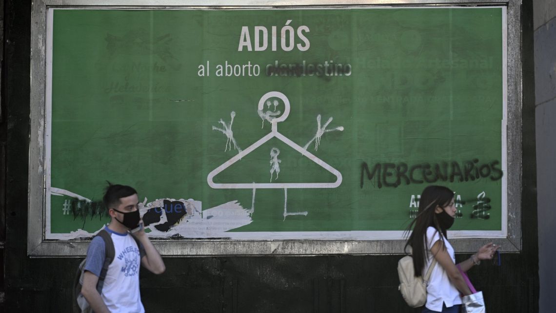 Commuters wait at a bus stop in front of a an advertise banner of Amnesty International supporting a bill to legalise abortion in Buenos Aires on December 17, 2020. 