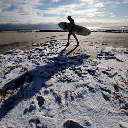 Un hombre camina por la playa para surfear en Long Beach, Nueva York. | Foto:Al Bello / Getty Images / AFP