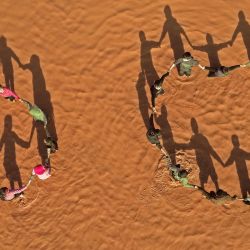 Esta fotografía muestra una vista aérea de niños parados juntos tomados de la mano en círculos en un estanque de agua de lluvia en el campamento inundado  | Foto:Omar Haj Kadour / AFP