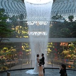 Una pareja de recién casados posa para su fotógrafo contra el Rain Vortex en Changi Jewel en Singapur. | Foto: Roslan Rahman / AFP