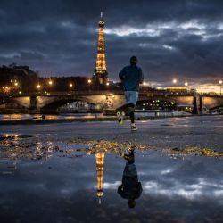 La Torre Eiffel se refleja en un charco mientras un hombre corre, en París. | Foto:Martin Bureau / AFP