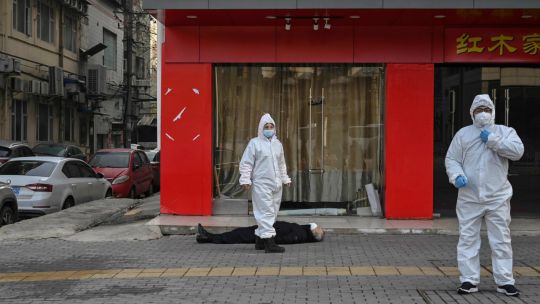 FOTO HISTÓRICA. Personal de emergencia revisa el cuerpo de un hombre que colapsó y murió en la calle en Wuhan el 26 de diciembre de 2019.