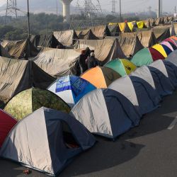 Los agricultores caminan frente a sus tiendas de campaña en una carretera bloqueada durante una protesta contra las recientes reformas agrícolas del gobierno central en Ghaziabad, a lo largo de la frontera estatal de Delhi-Uttar Pradesh. | Foto:Prakash Singh / AFP