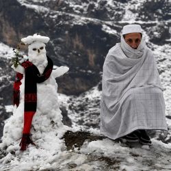 Un hombre se sienta junto a un muñeco de nieve después de las primeras nevadas en Landi Kotal. | Foto:Abdul Majeed / AFP