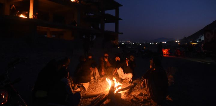 Los dolientes de una comunidad chiíta hazara se calientan alrededor de un fuego cerca de los ataúdes de los mineros que murieron en un ataque de hombres armados en el área montañosa de Machh, durante una sentada de protesta en el bypass oriental, en las afueras de Quetta.