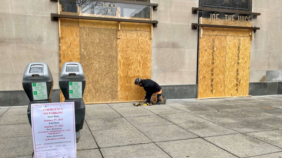 Operarios colocan protecciones en comercios cercanos a la manifestación de mañana.