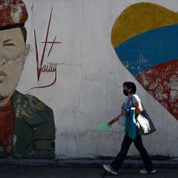 Una mujer con una máscara facial camina junto a una pared pintada que representa al fallecido presidente venezolano Hugo Chávez, en Caracas. | Foto:Federico Parra / AFP