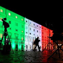 Una vista en Roma muestra a periodistas en video que trabajan fuera del Palazzo Chigi, la sede del gobierno italiano, iluminados con los colores de la bandera italiana, ya que se espera que el gobierno de Italia discuta más tarde una recuperación del coronavirus de 220 mil millones de euros. paquete de gastos. | Foto:Vincenzo Pinto / AFP