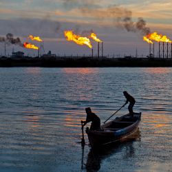Los pescadores iraquíes remaban en su bote a través de las pilas de bengalas que arden en el campo de Nahr Bin Omar, al norte del puerto de Basora, en el sur de Irak. | Foto:Hussein Faleh / AFP
