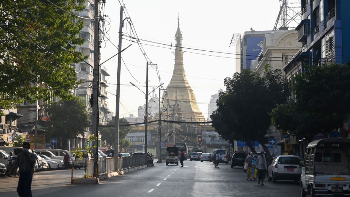 People walk next to the Sule Pagoda on an empty road in central Yangon on February 1, 2021, as Myanmar's military detained the country's de facto leader Aung San Suu Kyi and the country's president in a coup. 