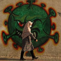 Una mujer palestina, con una máscara protectora en medio de la pandemia de COVID-19, pasa frente a un mural inspirado en el coronavirus en la ciudad de Gaza. | Foto:Mohammed Abed / AFP