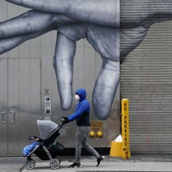 Una persona usa una mascarilla mientras empuja un cochecito de bebé frente a un mural de una mano en el muelle de carga en el Upper East Side de la ciudad de Nueva York el Día de los Presidentes. | Foto:Timothy A. Clary / AFP