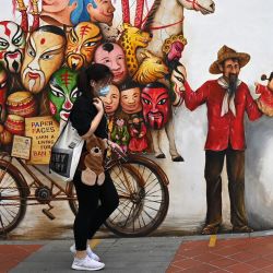 Una mujer pasa junto a un mural en una pared a lo largo de una calle en Singapur. | Foto:Roslan Rahman / AFP