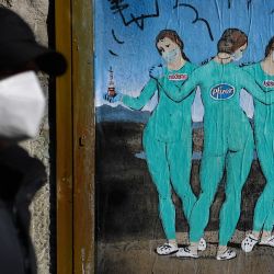 Un hombre con mascarilla pasa junto a una nueva obra del artista callejero italiano TvBoy titulada  | Foto:Josep Lago / AFP