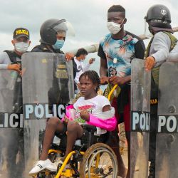 La policía abre el camino a una mujer en silla de ruedas mientras una multitud de migrantes de nacionalidades mixtas intentan cruzar a Perú por el Puente de la Amistad en la frontera con Brasil, a 1.600 kilómetros al sureste de Lima. | Foto:AFP