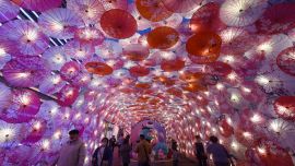 Muestra a personas que pasan junto a una exhibición de paraguas decorados con luces para el próximo Festival de los Faroles en una calle comercial en Hangzhou, en la provincia de Zhejiang, en el este de China.
