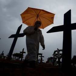 Un trabajador vestido con traje protector y portando un paraguas pasa junto a las tumbas de las víctimas del COVID-19 en el cementerio de NossaSenhora Aparecida, en Manaus, Brasil superó las 250.000 muertes por COVID-19. | Foto:afp