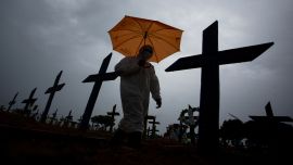 Un trabajador vestido con traje protector y portando un paraguas pasa junto a las tumbas de las víctimas del COVID-19 en el cementerio de NossaSenhora Aparecida, en Manaus, Brasil superó las 250.000 muertes por COVID-19.