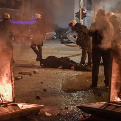 La policía se para cerca de contenedores de basura en llamas mientras su colega herido yace en la calle durante los enfrentamientos con los manifestantes en una manifestación contra la violencia policial en un suburbio de Atenas. | Foto:Louisa Gouliamaki / AFP