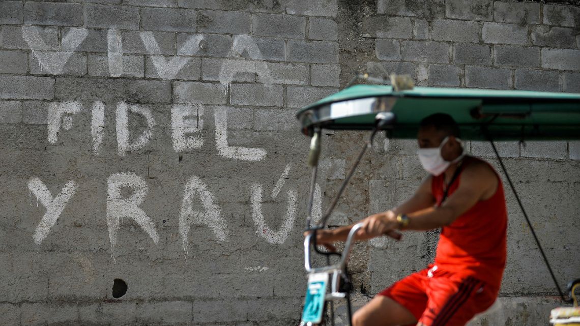 A man rides on his bicitaxi by a graffiti reading "Long Live Fidel and Raúl" in Havana, on March 15, 2021. 