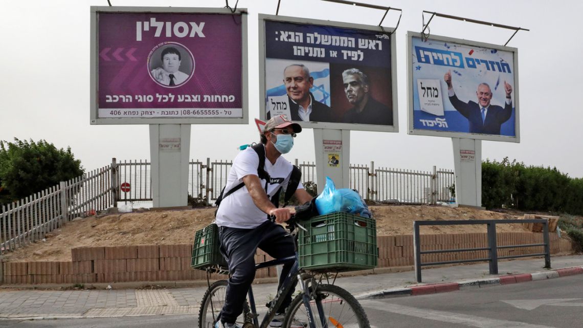 A man cycles across a street near electoral billboards of the Israeli Likud party showing (R to L) its leader Benjamin Netanyahu giving two thumbs up with text in Hebrew reading "returning to smile"; and another showing Netanyahu next to his opponent Yair Lapid with text reading "next Prime Minister: Lapid or Netanyahu", in the southern Israeli city of Beersheba on March 22, 2021, a day ahead of the fourth national election in two years. 