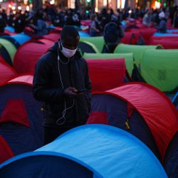Un hombre mira su teléfono móvil mientras se encuentra entre una de las 300 tiendas de campaña instaladas en La Place de la Republique para el inicio de una noche de solidaridad organizada por Collectif Requisitions para resaltar la difícil situación de las personas sin hogar en el centro de París. | Foto:Thomas Samson / AFP