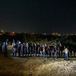 Los inmigrantes que llegaron ilegalmente a través del río Grande desde México hacen fila en un puesto de control de procesamiento antes de ser detenidos por agentes de la patrulla fronteriza en la ciudad fronteriza de Roma. | Foto:Ed Jones / AFP