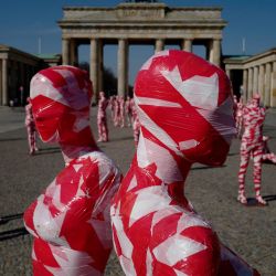 Maniquíes envueltos en cinta de barrera se colocan frente a la histórica Puerta de Brandenburgo de Berlín, como parte del Monumento a la Corona del artista alemán Dennis Josef Meseg llamado  | Foto:John Macdougall / AFP