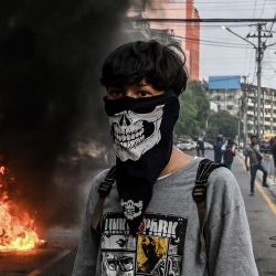 Un manifestante con el rostro cubierto se encuentra cerca de una barricada improvisada en llamas a lo largo de una carretera durante una protesta contra el golpe militar, en Yangon. | Foto:STR / AFP