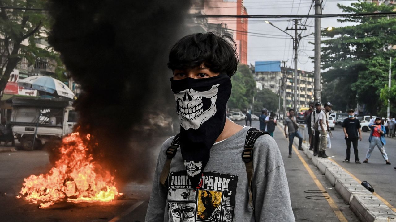 Un manifestante con el rostro cubierto se encuentra cerca de una barricada improvisada en llamas a lo largo de una carretera durante una protesta contra el golpe militar, en Yangon. | Foto:STR / AFP