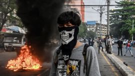 Un manifestante con el rostro cubierto se encuentra cerca de una barricada improvisada en llamas a lo largo de una carretera durante una protesta contra el golpe militar, en Yangon.