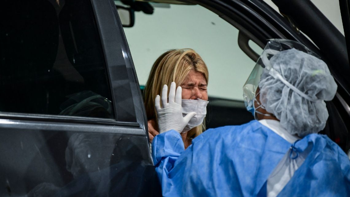 A health worker collects samples for Covid-19 coronavirus case detection testing inside a car at the Costa Salguero convention centre, in Buenos Aires, on April 5, 2021. 