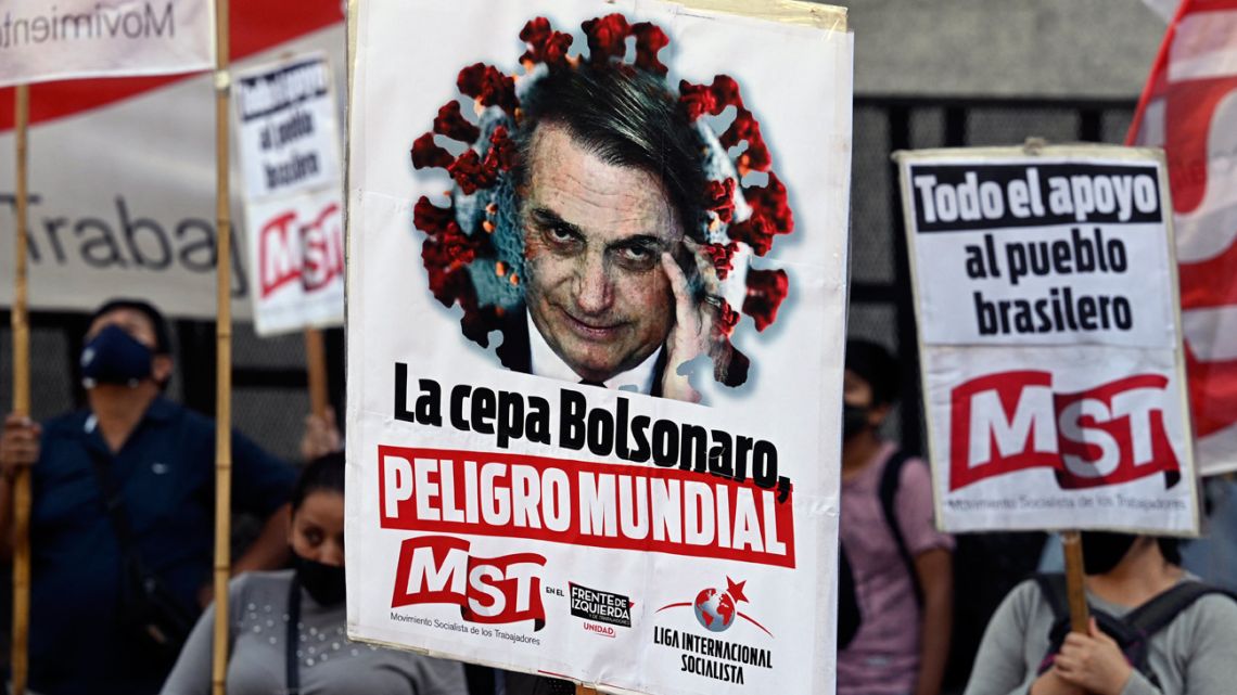 People hold banners depicting Brazil's President Jair Bolsonado reading "The Bolsonaro strain, world danger" during a protest of members of leftist parties outside the Brazilian Embassy in Buenos Aires, on April 14, 2021, amid the coronavirus pandemic. 