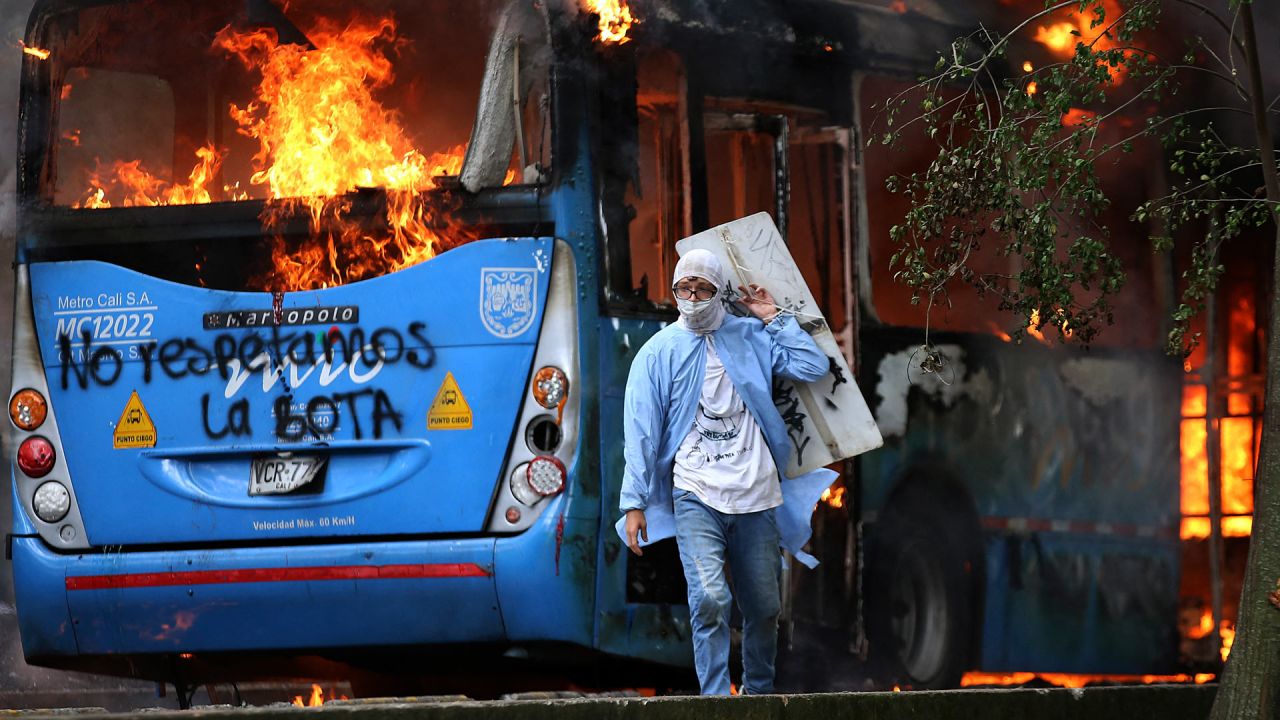 Un hombre camina frente a un autobús de transporte público en llamas durante una protesta contra un proyecto de reforma tributaria lanzado por el presidente colombiano Iván Duque, en Cali. | Foto:Paola Mafla / AFP