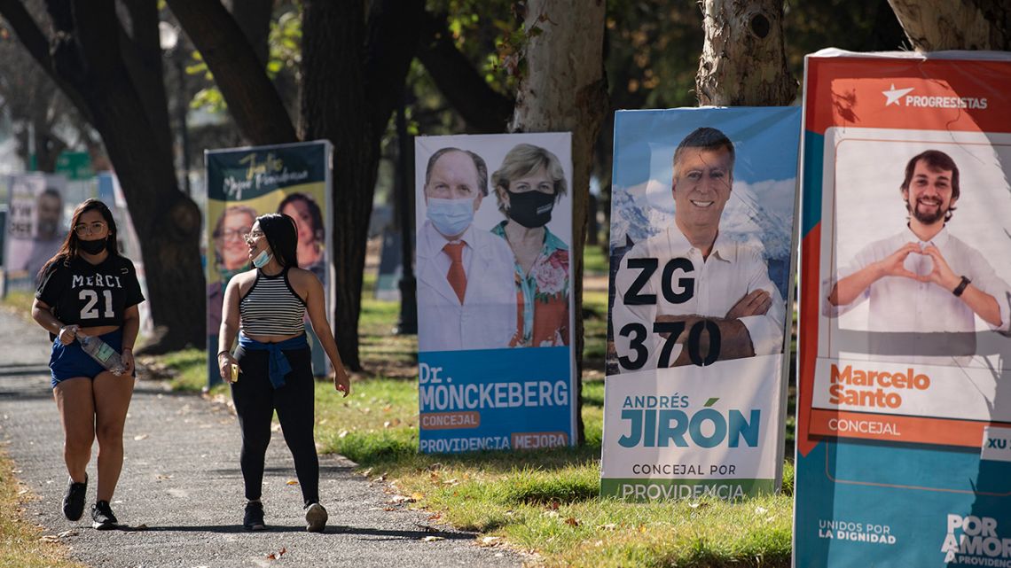 Women walk past electoral propaganda in Santiago, on May 12, 2021, ahead of May 15 and 16 elections to choose mayors, councillors and a commission to rewrite the constitution.