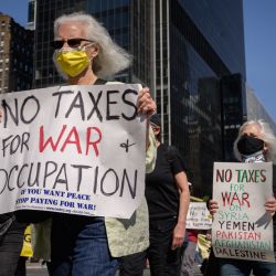 Los manifestantes sostienen carteles para pedir el fin de los impuestos federales sobre la renta que se utilizan para gastos militares mientras marchan por una calle frente al edificio Empire State en la ciudad de Nueva York. | Foto:Ed Jones / AFP