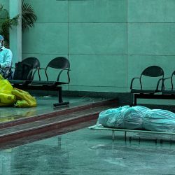 Trabajadores de la salud con trajes de Equipo de Protección Personal (EPP) se sientan junto al cadáver de una persona que murió debido al coronavirus Covid-19, en un crematorio en Nueva Delhi. | Foto:Prakash Singh / AFP