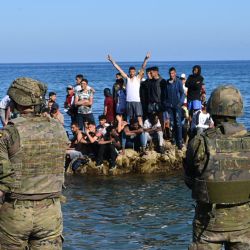 Los soldados españoles montan guardia mientras los migrantes se paran en las rocas frente a la costa del enclave español de Ceuta. - España aumentó la presión diplomática sobre Rabat cuando su primer ministro voló a Ceuta, prometiendo  | Foto:Antonio Sempere / AFP
