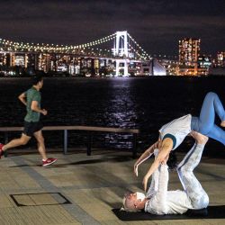 Un corredor pasa corriendo junto a personas que practican yoga en un parque en el área de la bahía de Tokio. | Foto:Charly Triballeau / AFP