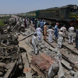 Un tren de pasajeros pasa junto a los restos de un tren en Daharki, un día después de que un tren interurbano lleno se estrellara contra otro expreso que descarriló y mató al menos a 63 personas. | Foto:Asif Hassan / AFP