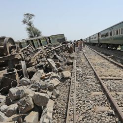 Los pasajeros miran por la ventana de un tren mientras viajan junto a los restos de un tren después de una restauración de la vía férrea en Daharki, un día después de que un tren interurbano lleno se estrellara contra otro expreso. que se había descarrilado, matando al menos a 63 personas. | Foto:Shahid Saeed Mirza / AFP